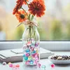 A glass bottle filled with colorful water beads and orange flowers sits on a windowsill. Produktbild-Vorschau
