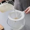A person is pouring liquid from a glass pitcher through a white mesh strainer into a glass bowl. Produktbild-Vorschau
