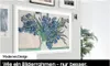 A framed television displaying a painting of blue irises on a wall, with a plant to the right. Voir les images du produit