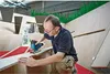 A man is using a jigsaw to cut a piece of wood in a workshop or construction setting. Voir les images du produit