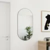 A mirror is hanging on a white wall next to a door and a framed picture. A plant is reflected in the mirror. Náhľad obrázku produktu