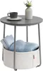 A round gray side table with a storage basket underneath, holding books and a blue blanket. Produktbild-Vorschau