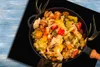 A close-up overhead view of a pan filled with cooked vegetables, placed on a black surface with deer antlers and a deer head graphic. Produktbild-Vorschau