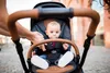 A baby sitting in a stroller, with a person's hands visible adjusting the stroller. Náhled obrázku produktu