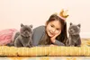 A young girl wearing a crown is lying on a yellow cushion with two stuffed cats. Voir les images du produit