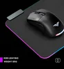 A black wireless gaming mouse with RGB lighting is placed on a black mousepad with RGB lighting. A small grey rectangular device is also visible on the mousepad. Produktbild-Vorschau