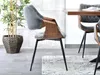 A modern dining chair with a wooden frame and gray upholstery is placed next to a dining table. A large potted plant is visible in the background. Náhled obrázku produktu