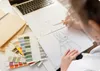 A person is drawing a high chair design on paper, with color swatches and a laptop nearby. Voir les images du produit