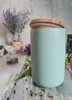 A turquoise ceramic storage jar with a wooden lid sits on a weathered wooden surface, surrounded by scattered peppercorns and greenery. In the background, there are decorative elements like dried lavender and a small jar. Náhľad obrázku produktu