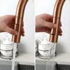 A split image showing a hand operating a copper-colored kitchen faucet. The left side shows a single stream of water, while the right side shows a spray pattern. Podgląd zdjęcia produktu