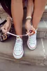 A person tying the laces of white sneakers with red trim. Voir les images du produit
