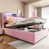 A pink upholstered bed with storage is shown with the mattress lifted, revealing the storage compartment. The bed has a tufted headboard with LED lighting and a digital clock. Náhled obrázku produktu
