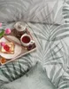 A breakfast tray with toast, jam, tea, and tulips on a bed with a leaf pattern. Anteprima dell’immagine prodotto