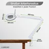 A white magnifying lamp with an adjustable arm is clamped to a wooden table, with dimensions indicated by green lines and text. Produktbild-Vorschau