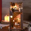 A miniature, illuminated dollhouse-like structure resembling a bookshelf insert, with detailed interior scenes and furniture, set against a dark, textured background. Voir les images du produit