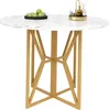 A round dining table with a marble-effect top and gold geometric legs, shown from a front-facing angle against a white background. There are green apples in a black bowl and some decorative items on the table. Voir les images du produit