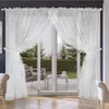 A white sheer curtain with lace trim is displayed across a sliding glass door, revealing a garden view. Produktbild-Vorschau