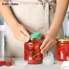 A person is shown sealing a jar of pickled red peppers with a green lid. Another sealed jar is visible in the background. Small white paper liners are also present on the table. Produktbild-Vorschau