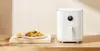 A white air fryer sits on a wooden surface next to a plate of french fries and a lemon. Podgląd zdjęcia produktu