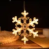 A lit snowflake decoration hangs against a dark background, with a textured surface and wooden planks visible below. Produktbild-Vorschau