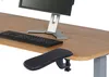 A close-up view of an ergonomic armrest attached to the edge of a wooden desk, with a computer monitor and keyboard visible in the background. Podgląd zdjęcia produktu