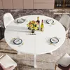 A white round dining table set for a meal with flowers and wine bottles. Náhled obrázku produktu