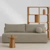 A modern sofa with a wooden bookshelf in the background and a small side table with a mug. Produktbild-Vorschau