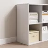 A white cube shelf unit with books and boxes inside, placed against a wall. Produktbild-Vorschau