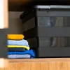 A stack of folded towels next to a black storage box on a wooden shelf. Anteprima dell’immagine prodotto