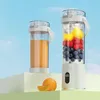 Two portable blenders are displayed on white and green platforms against a blue sky background. One blender contains orange juice, and the other contains fruits and ice. An orange and a slice of orange are placed in front of the blenders. Produktbild-Vorschau