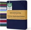 A folded navy blue fitted sheet is displayed, with a stack of other colored sheets in the background. A product tag and a cardboard band with product information are attached to the sheet. Produktbild-Vorschau