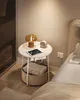 A bedside table with a lamp, tablet, and blanket beside a bed. Náhled obrázku produktu