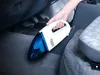 A hand is using a white and blue handheld vacuum cleaner to clean the floor of a car. Náhled obrázku produktu