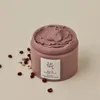 A jar of pinkish-red pore mask with red beans scattered around it on a light gray background. Produktbild-Vorschau