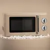 A retro-style beige microwave oven is displayed on a light beige surface, surrounded by popcorn. Produktbild-Vorschau