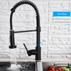 A black kitchen faucet with a pull-out spray head is shown in use, with water flowing into a sink. The background is a white brick wall. Náhled obrázku produktu