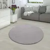A round, gray rug is placed on a light wooden floor in a living room setting, with a gray sofa and white furniture visible in the background. Produktbild-Vorschau