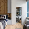A bedroom with a bed, wooden wall paneling, and a mirrored door reflecting a living area. Anteprima dell’immagine prodotto