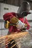 A person wearing protective gear is using a DeWalt angle grinder to cut metal, creating a shower of sparks. Voir les images du produit