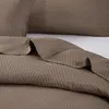 A close-up view of a brown quilted blanket with a geometric triangle pattern. Produktbild-Vorschau