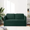 A dark green sofa bed is shown in a well-lit room with a plant on the left and a bookshelf on the right. Produktbild-Vorschau