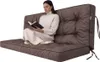 A woman sits on a brown floor cushion, reading a book. Náhled obrázku produktu