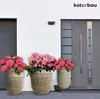 Three large planters with pink flowers are placed in front of a modern house with a gray door and garage door. Produktbild-Vorschau