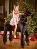 A young girl is riding a black rocking horse in front of a decorated Christmas tree and wrapped gifts. Anteprima dell’immagine prodotto