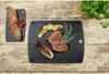 A black cutting board with grilled steak, vegetables, and rosemary, next to a smaller cutting board with bread and tomatoes, on a rustic wooden table. Náhľad obrázku produktu