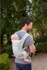A man is carrying a baby in a carrier on his back while walking outdoors. Anteprima dell’immagine prodotto