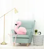 A plush flamingo sits in a light blue armchair next to a small table with a plant and an alarm clock. Produktbild-Vorschau