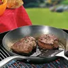 Two steaks are being cooked in a pan on a grill, with a red tablecloth and bread in the background. Voir les images du produit