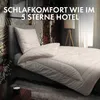 A neatly made bed with a white duvet and pillow, set against a decorative wallpaper and a lamp in the background. Produktbild-Vorschau