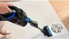 A person is using a cordless vacuum cleaner on a carpet. A close-up inset shows dirt particles on the carpet fibers. Náhled obrázku produktu